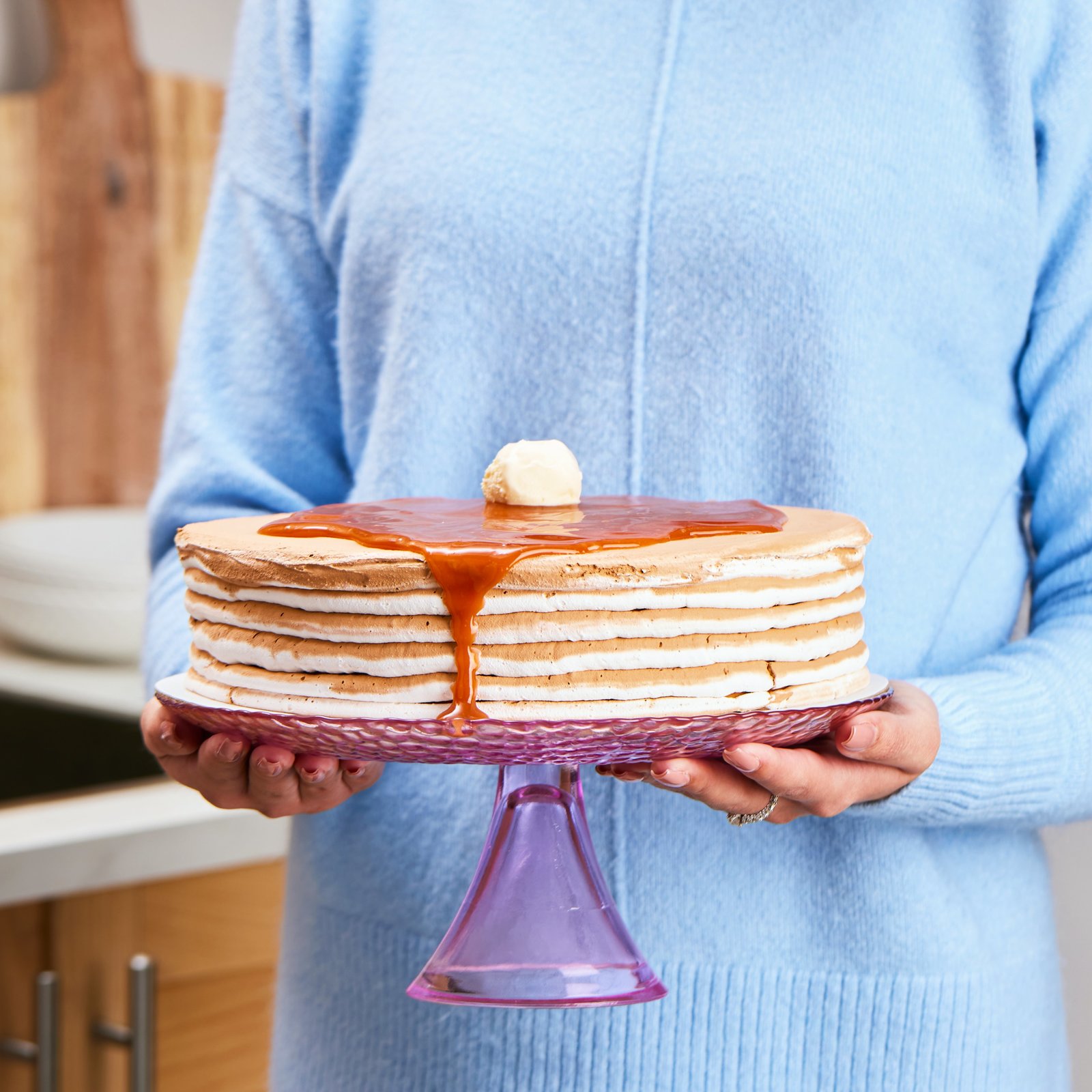 a woman holding a stack of pancakes covered in syrup