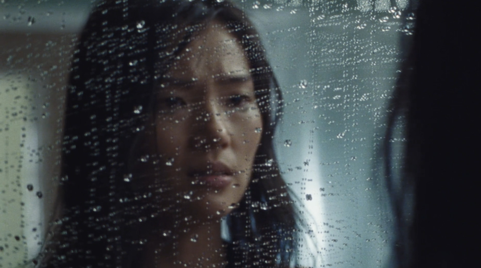 a woman standing in front of a window covered in rain