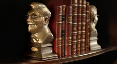 a bronze busturine of a man in front of a row of books