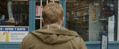 a man in a brown jacket walking past a store