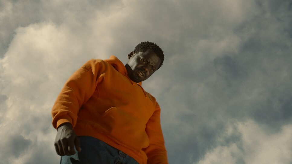 a man in an orange shirt standing in front of a cloudy sky