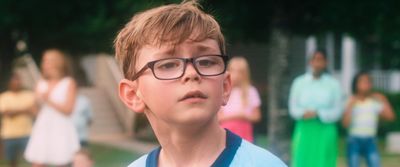 a young boy wearing glasses standing in front of a group of people