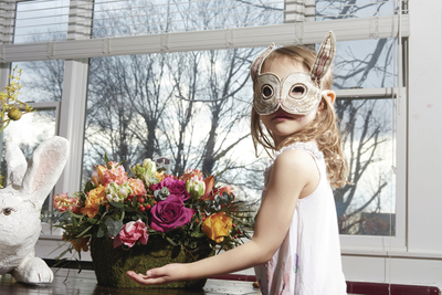 a little girl wearing a bunny mask next to a vase of flowers