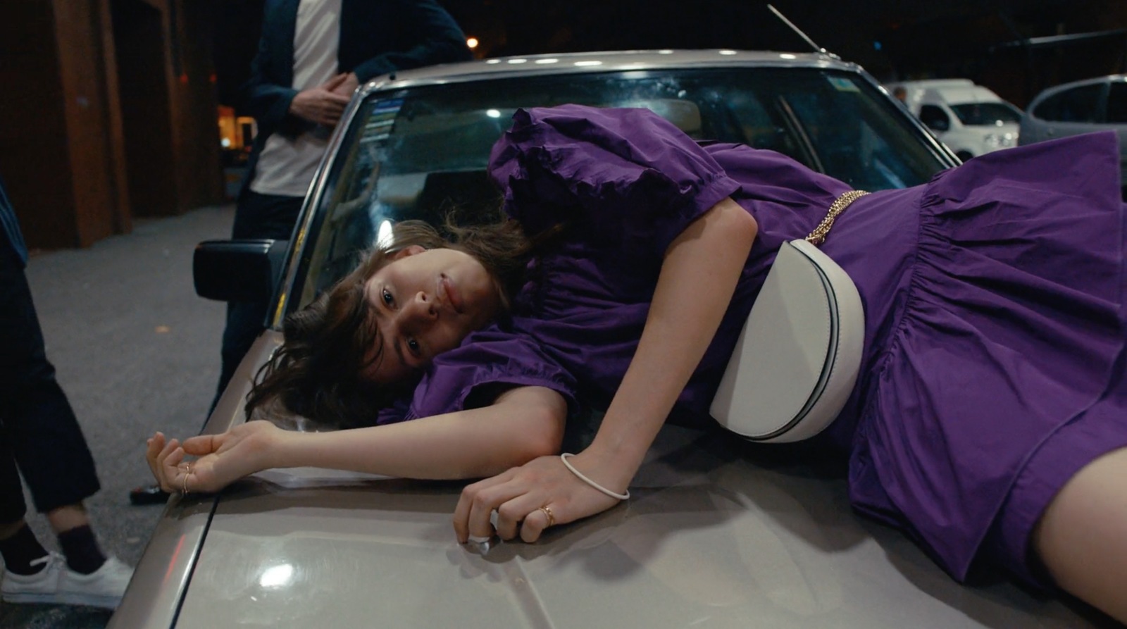 a woman in a purple dress laying on the hood of a car