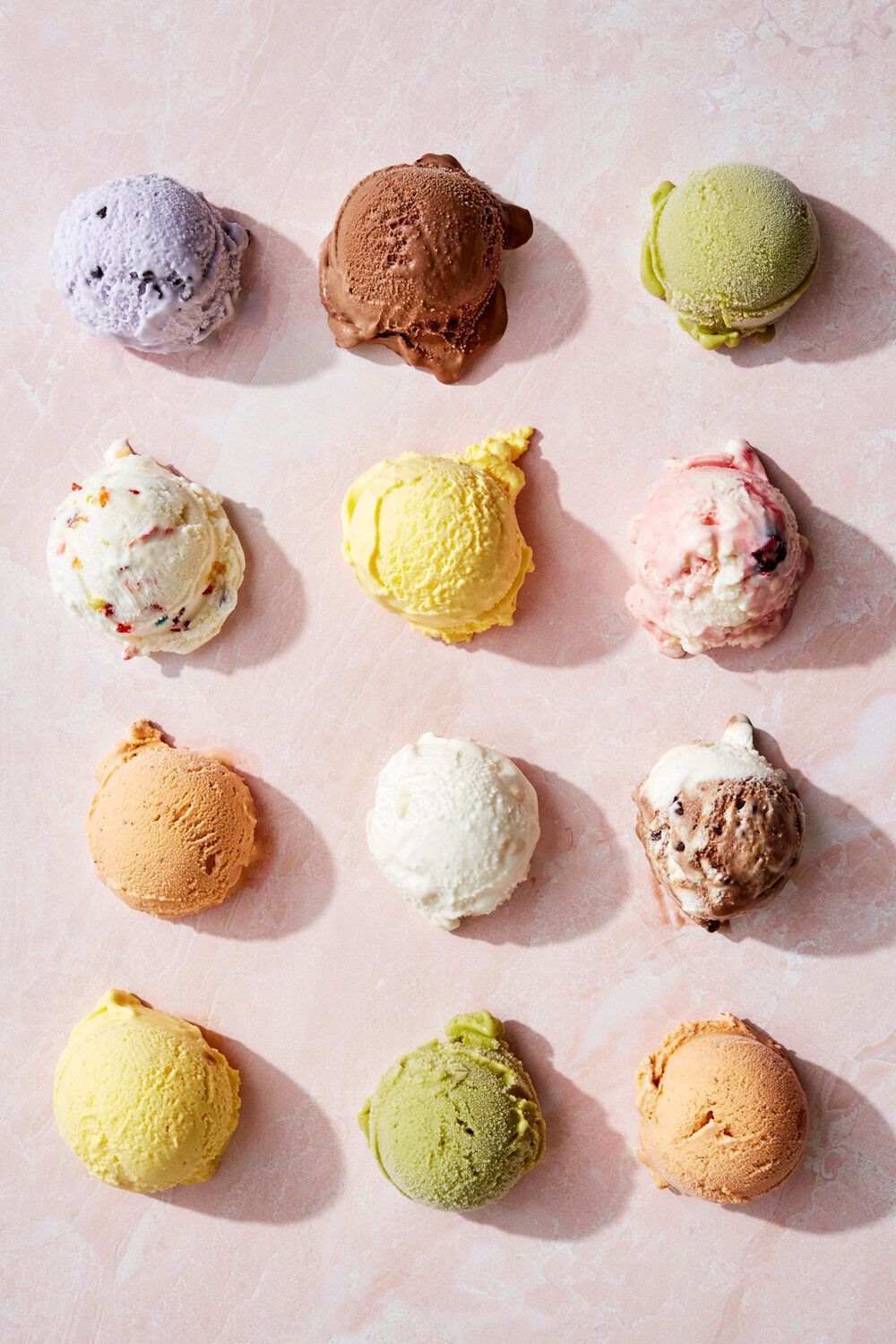 a bunch of different colored ice creams on a pink surface