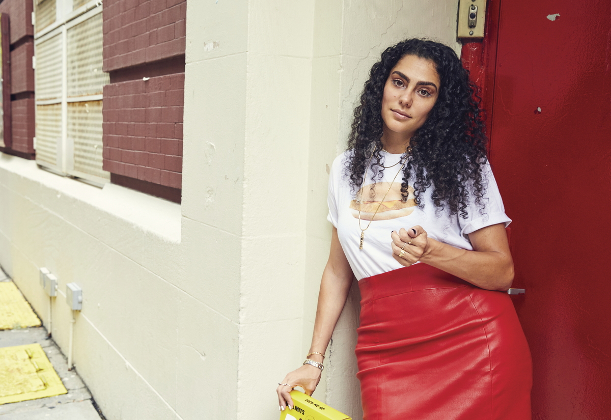 a woman leaning against a wall with a yellow purse