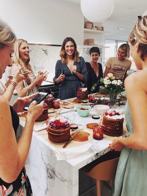 a group of women standing around a table with cakes on it