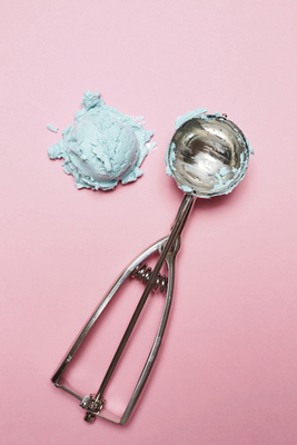 a scoop of blue paste next to a spoon on a pink background