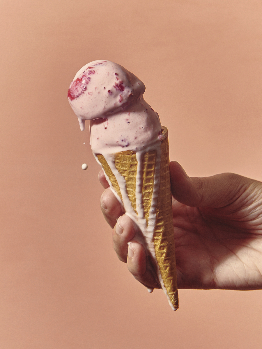 a hand holding an ice cream cone with pink icing