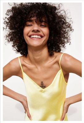 a woman with curly hair smiling and wearing a yellow top