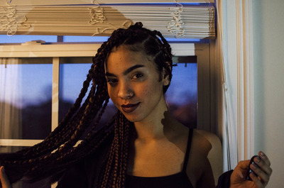 a woman with long braids standing in front of a window