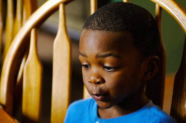 a young boy sitting in a wooden chair