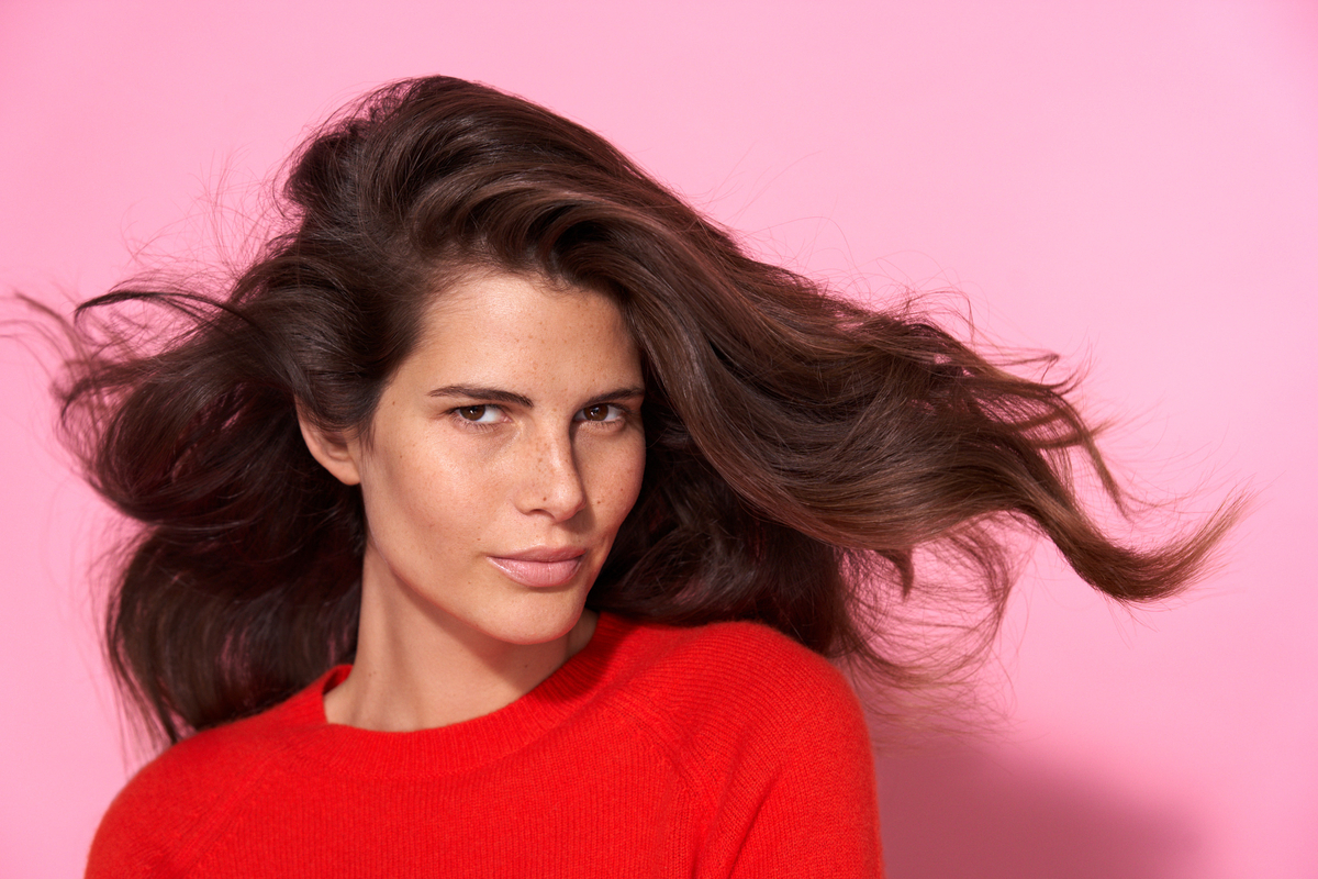 a woman in a red sweater blow drying her hair