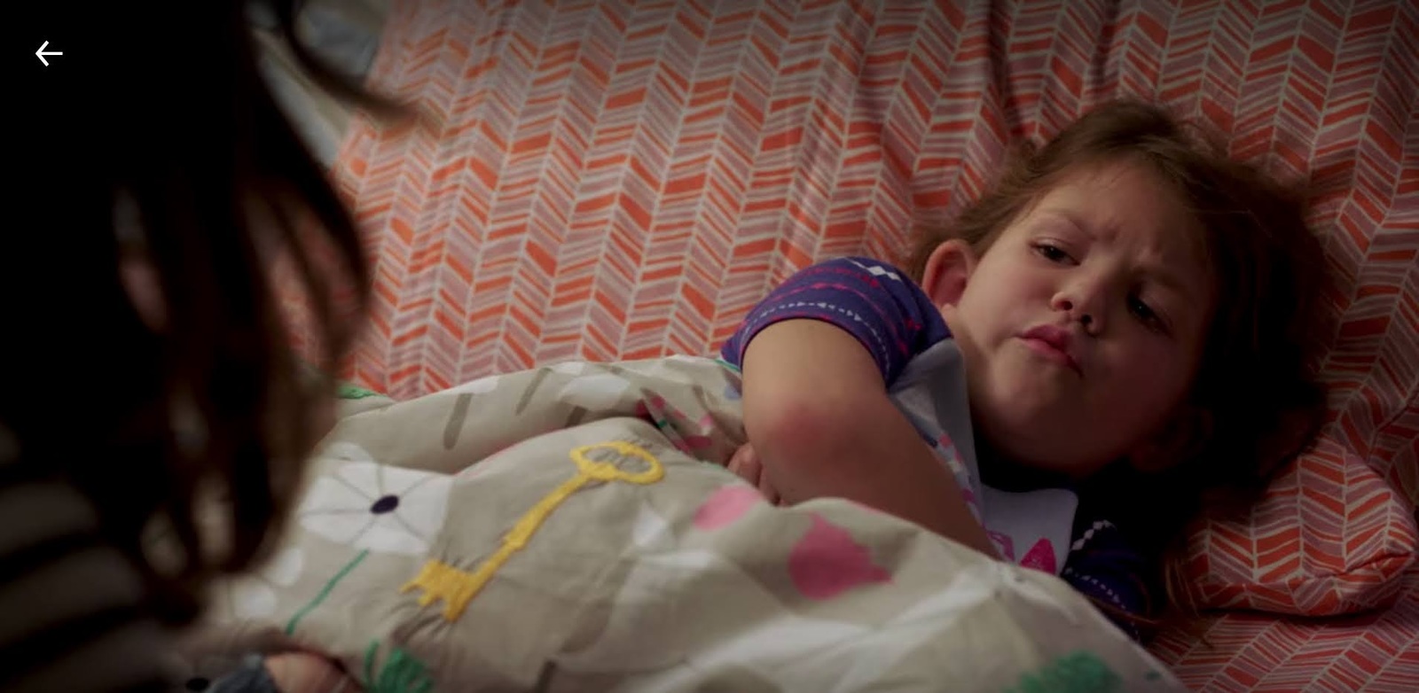 a little girl laying in bed with a blanket