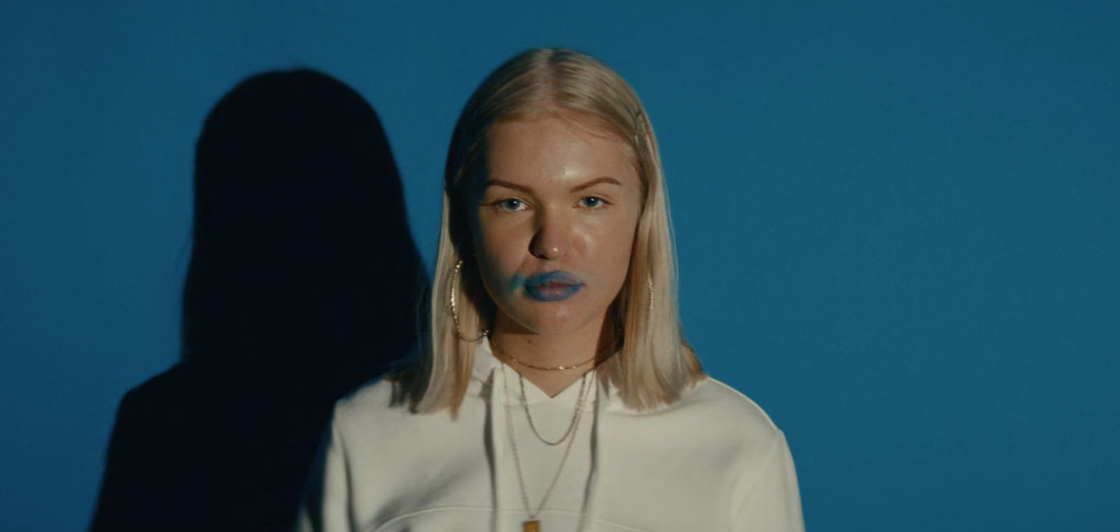 a woman with blue lipstick standing in front of a blue wall