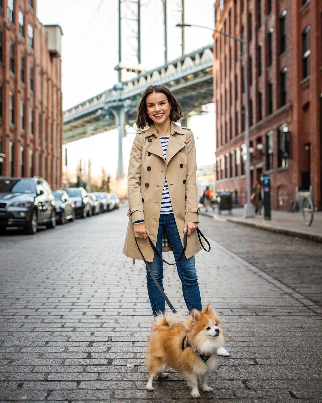 a woman in a trench coat is walking her dog