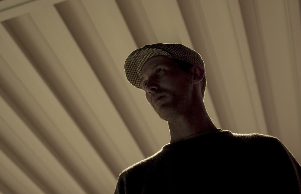 a man wearing a hat standing in front of a window