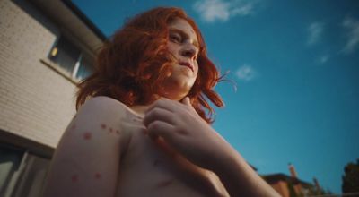 a woman with red hair standing in front of a house