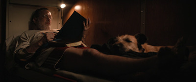 a man reading a book with a dog laying next to him