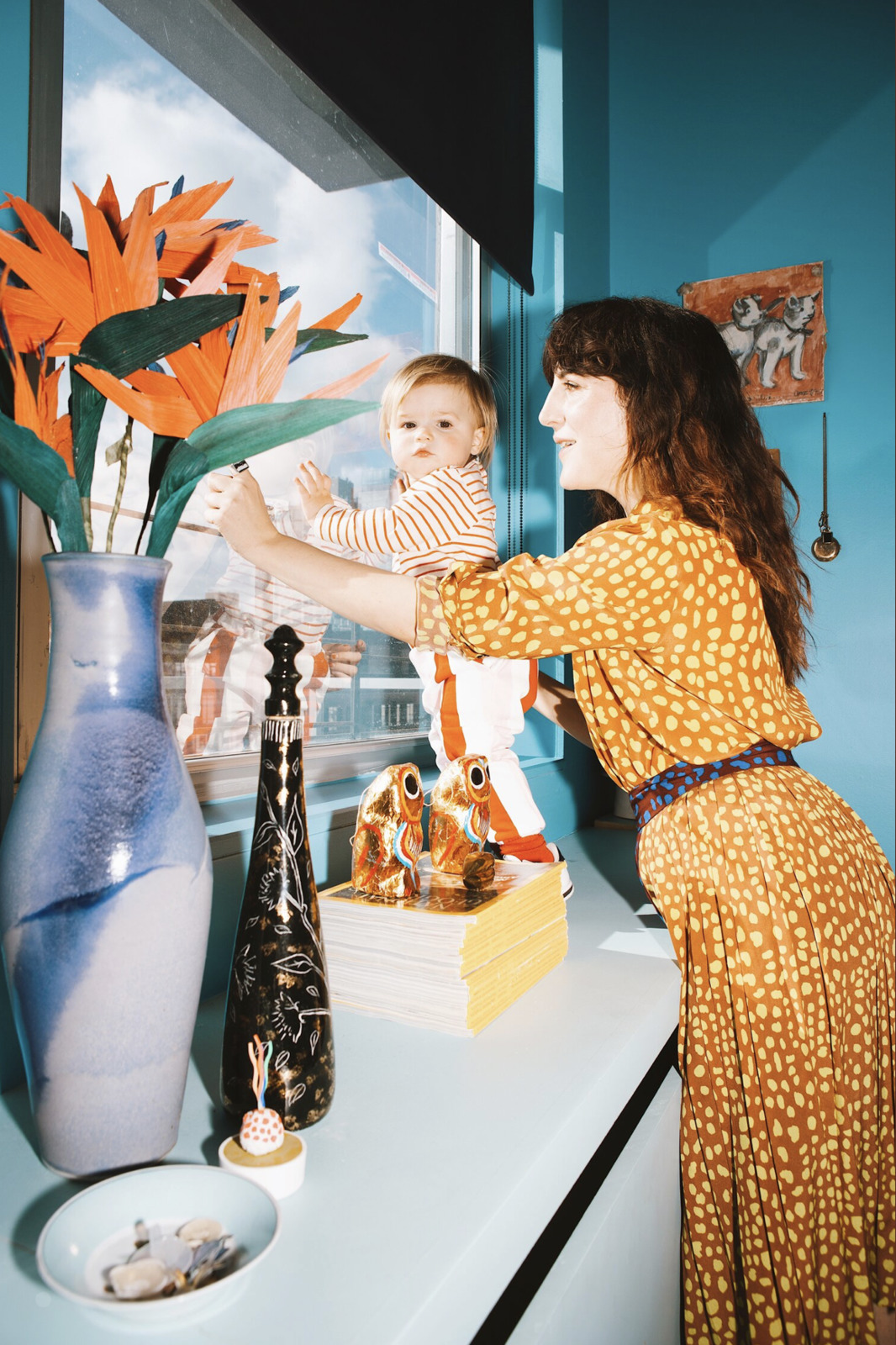 a woman holding a baby near a vase of flowers