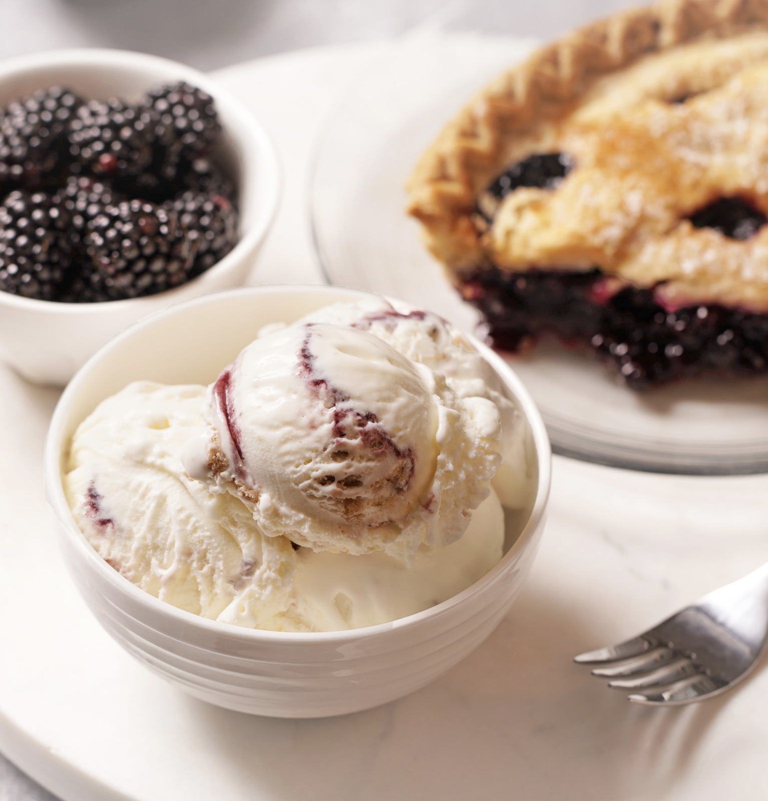 a white plate topped with a bowl of ice cream next to a pie