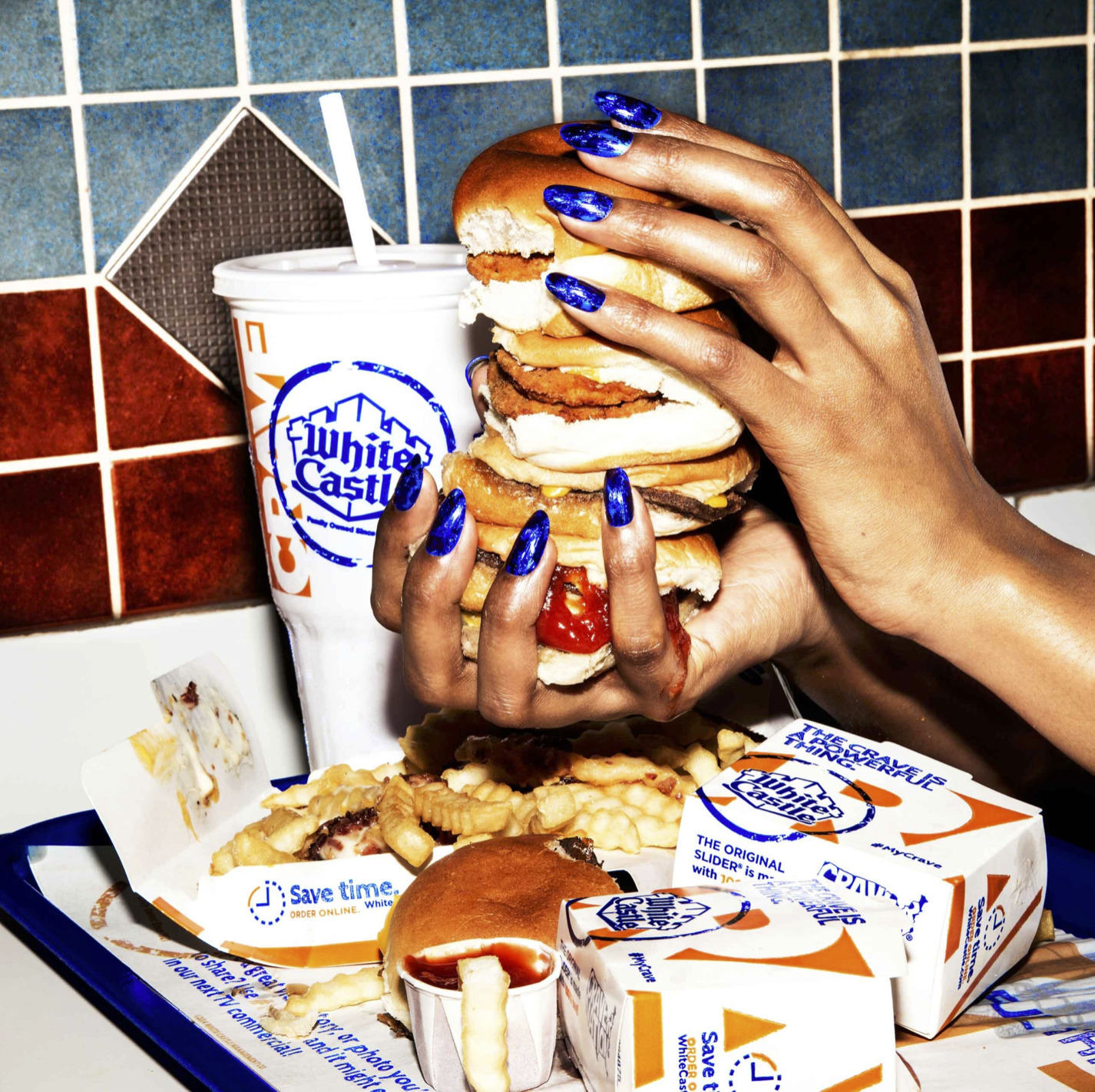 a woman holding a giant hamburger over a tray of food