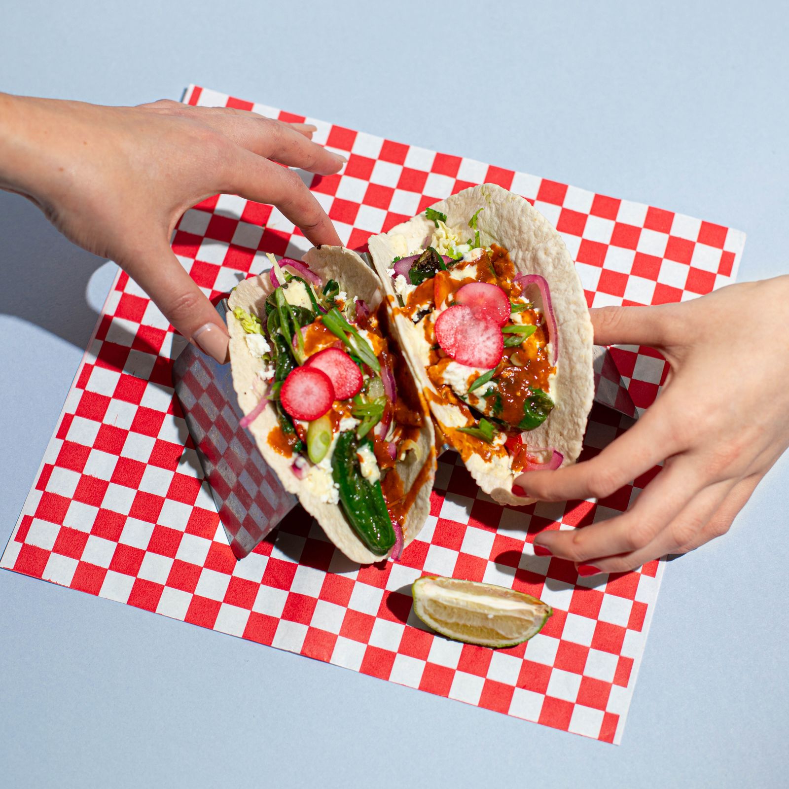 a person holding two tacos on top of a red and white checkered table