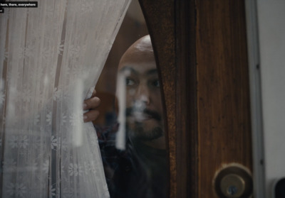 a man looking out of a window through a curtain