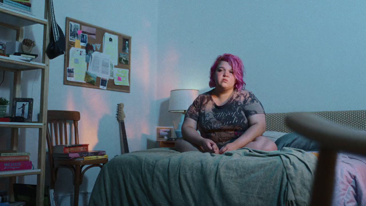 a woman with pink hair sitting on a bed