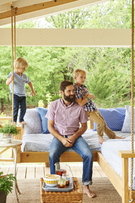 a man sitting on a porch swing with two children