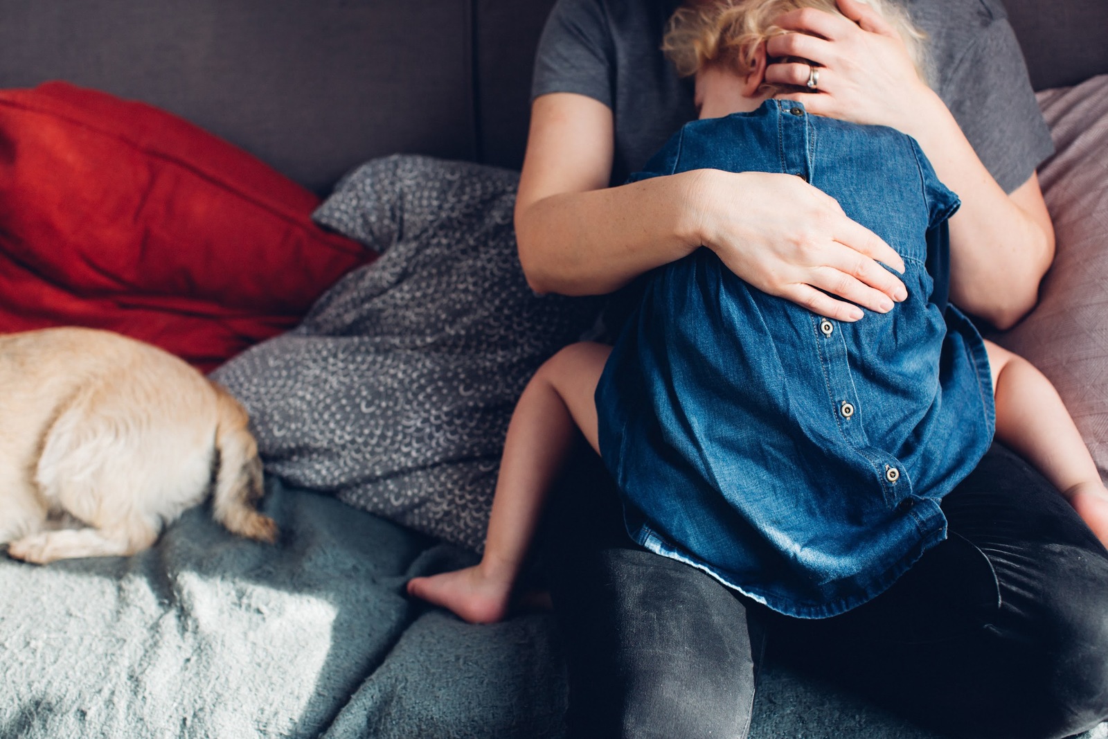 a woman sitting on a couch holding a baby next to a dog