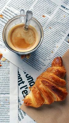 a croissant sitting on top of a newspaper next to a cup of coffee