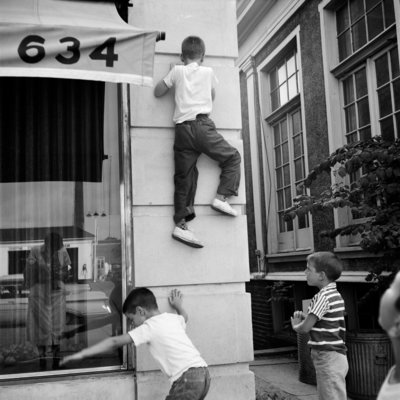 a black and white photo of two boys climbing a building