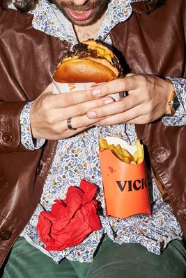 a man in a brown jacket holding a sandwich and a drink