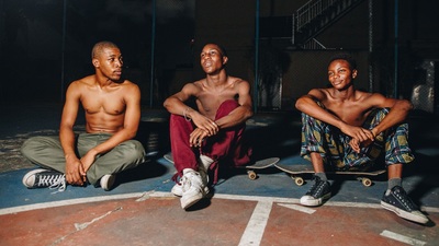 three men sitting on the ground with their skateboards