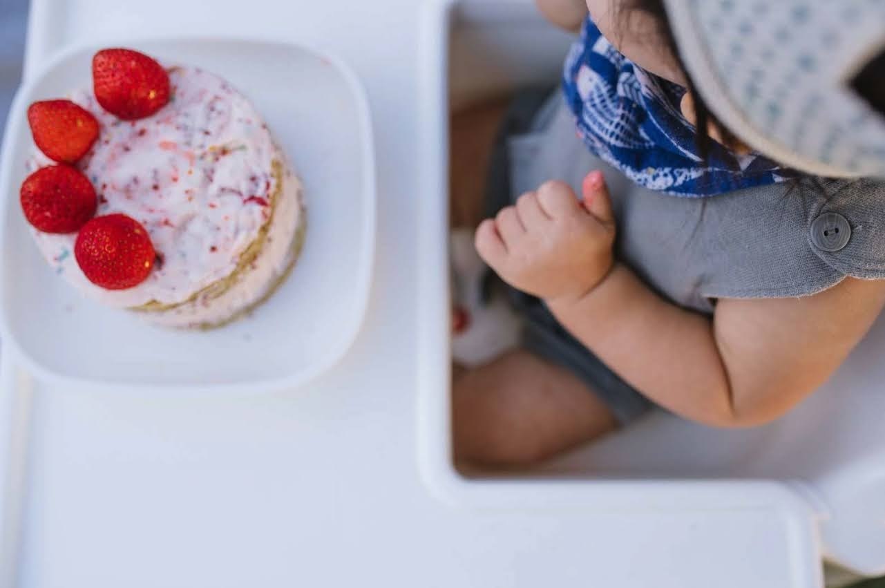 a small child sitting on a white table with a plate of food