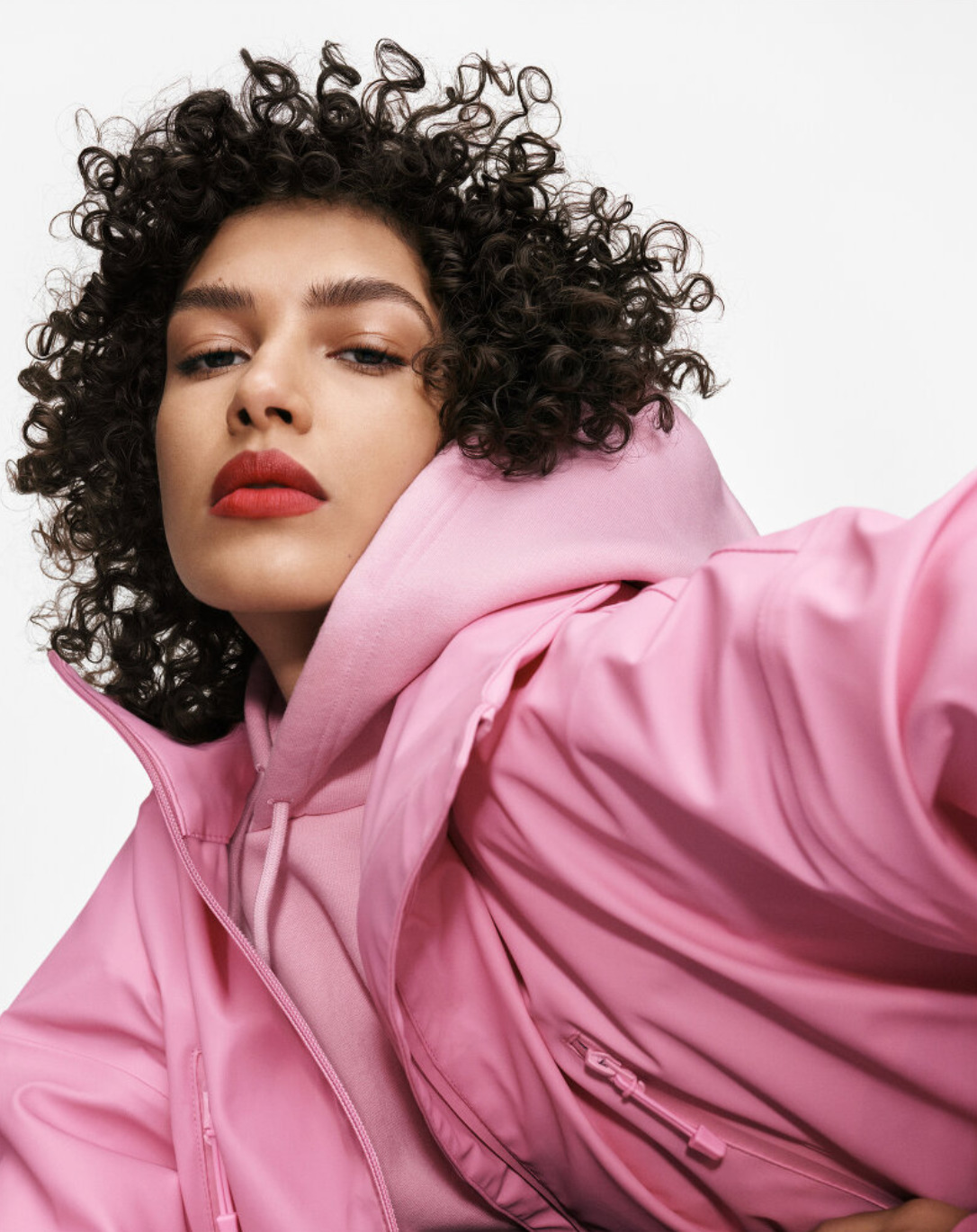 a woman with curly hair wearing a pink jacket