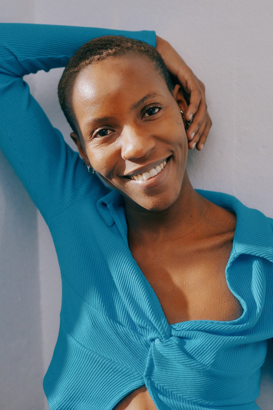 a smiling woman in a blue top leaning against a wall