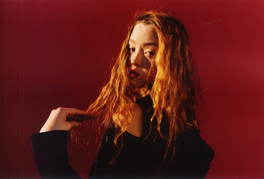 a woman with long red hair standing in front of a red background