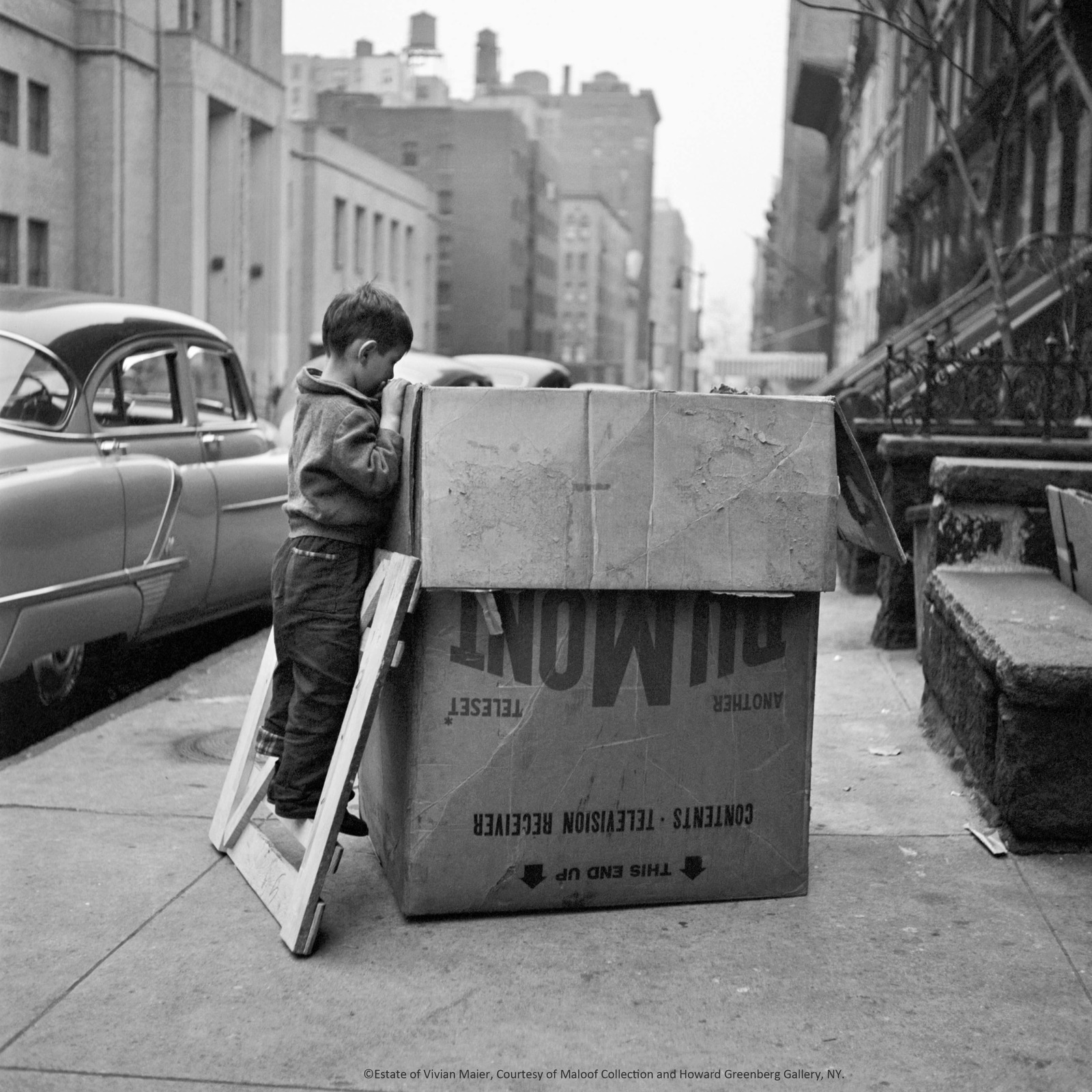 a young boy standing next to a box on a sidewalk