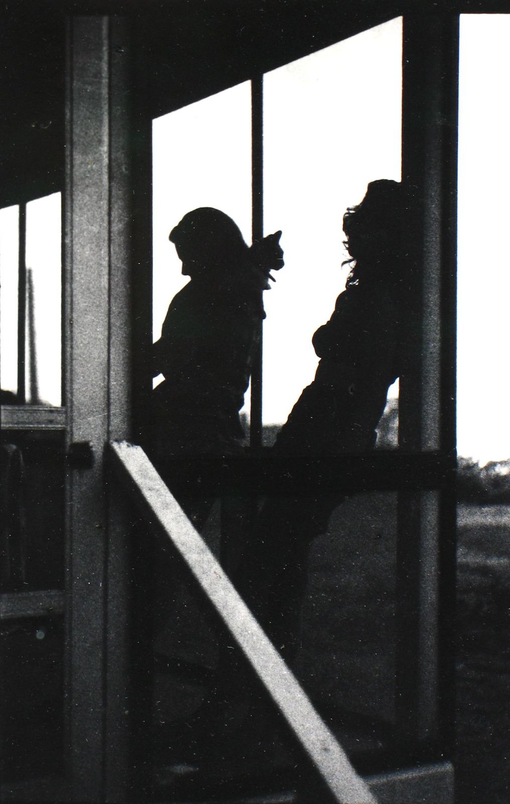 a black and white photo of two people looking out a window