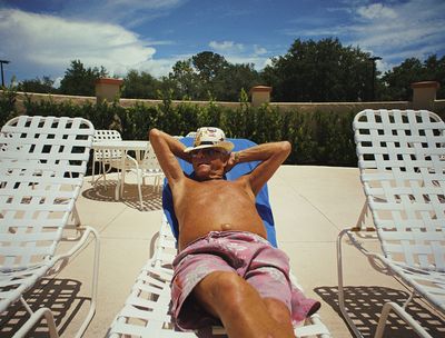 a man laying on top of a white lawn chair