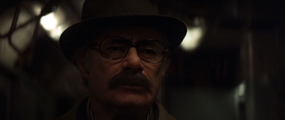 a man with glasses and a hat in a dark room