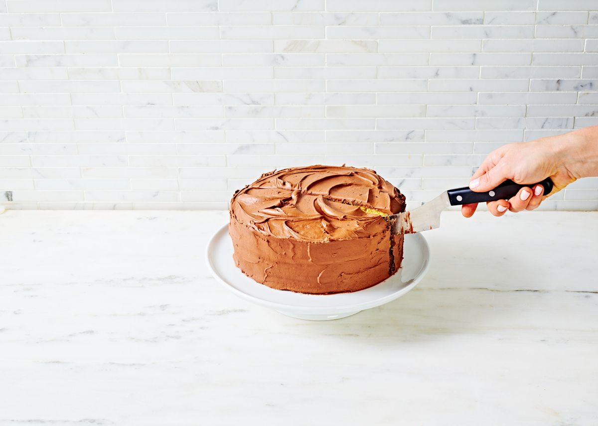 a person cutting a chocolate cake with a knife