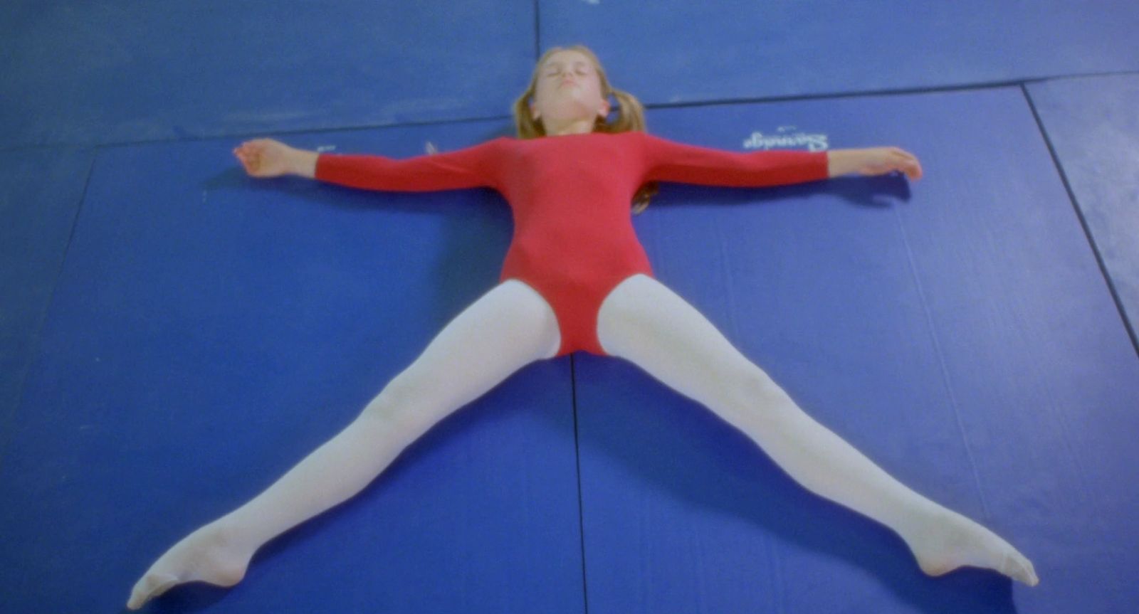 a girl in a red leotard laying on a blue mat