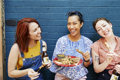 three women sitting on a bench eating food and drinking beer