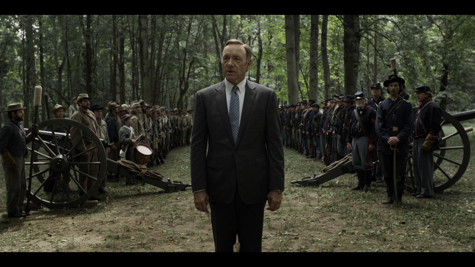 a man in a suit and tie standing in front of a line of soldiers