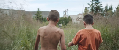 two young boys walking through tall grass towards a building