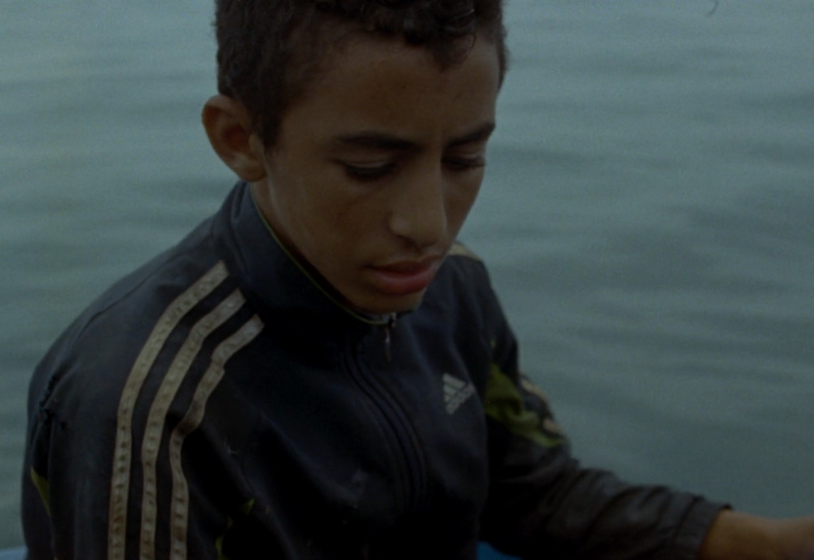 a young man standing next to a body of water