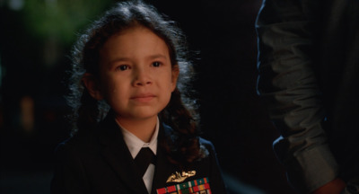 a little girl in a uniform standing next to a man